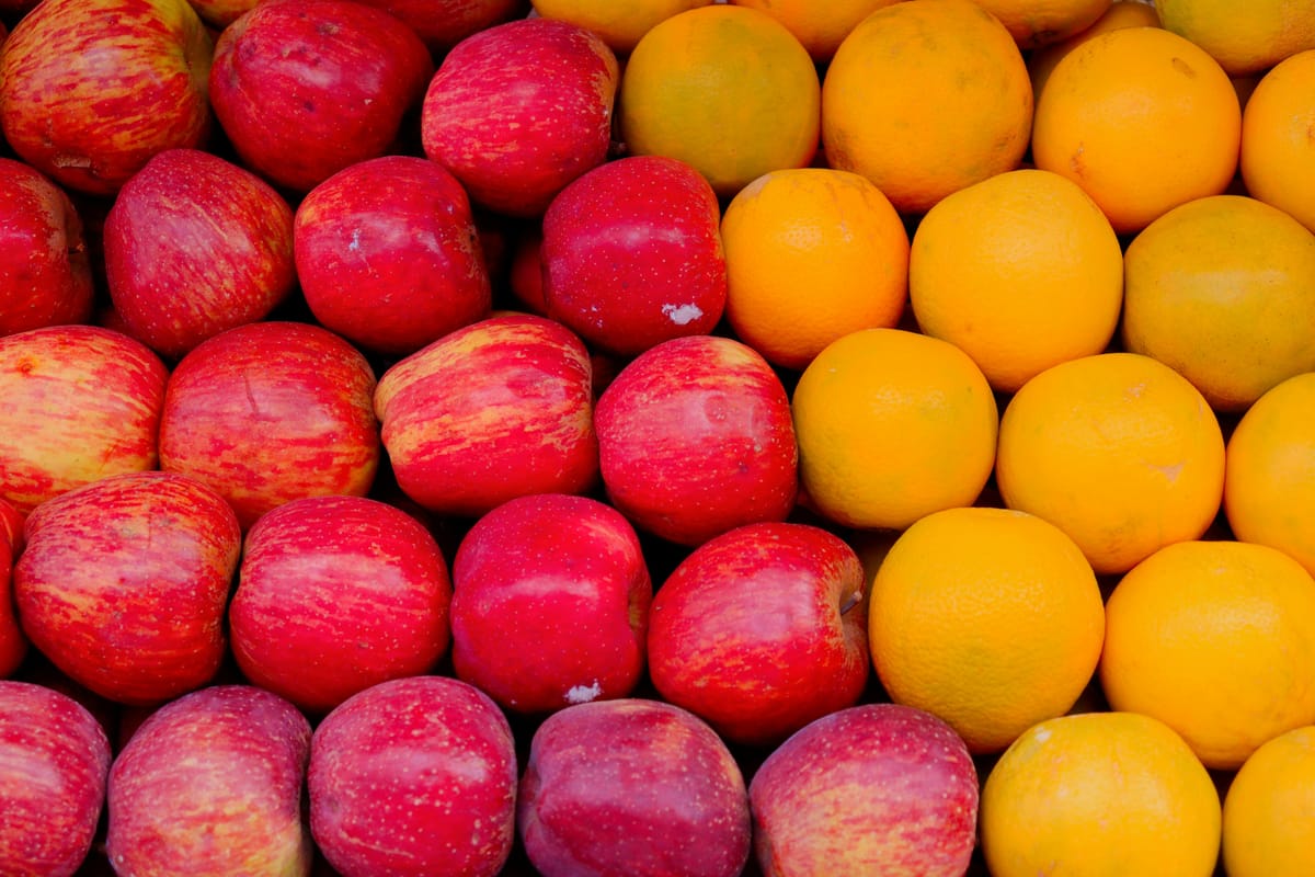 A tightly packed display of fruit arranged in rows, with shiny red apples filling the left side and bright yellow-orange citr
