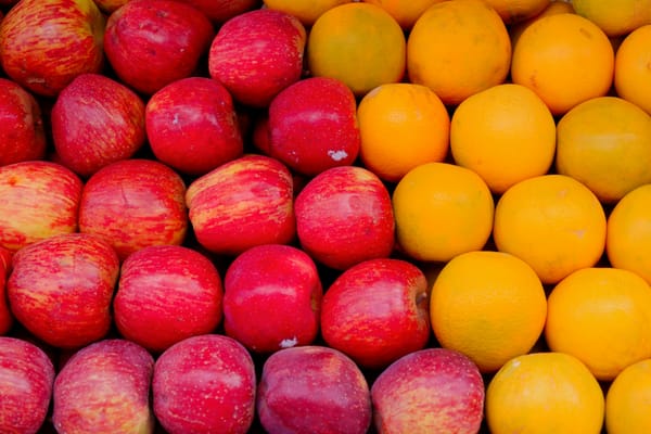A tightly packed display of fruit arranged in rows, with shiny red apples filling the left side and bright yellow-orange citr