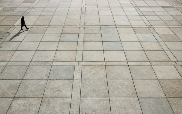A man in an overcoat works across a floor with square tiles.